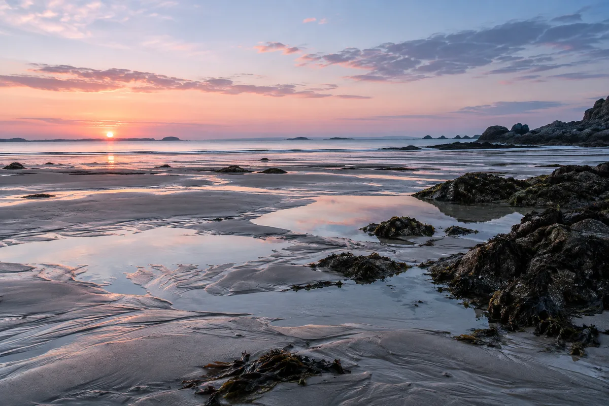 Plage bretonne déserte à l’aube, sable humide de marée basse sous un ciel pastel